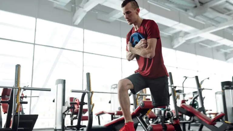 Man in de sportschool met zijn achterste voet op een bank en een halterschijf tegen zijn borst tijdens een split squat