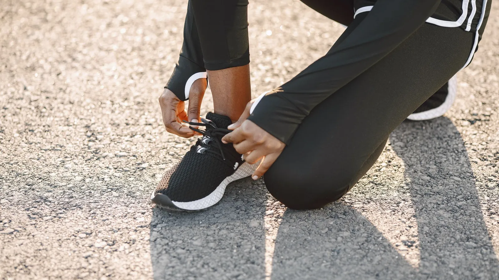 Sporter in zwarte trainingsbroek knielt op straat en strikt de veters van haar sportschoenen voor een training