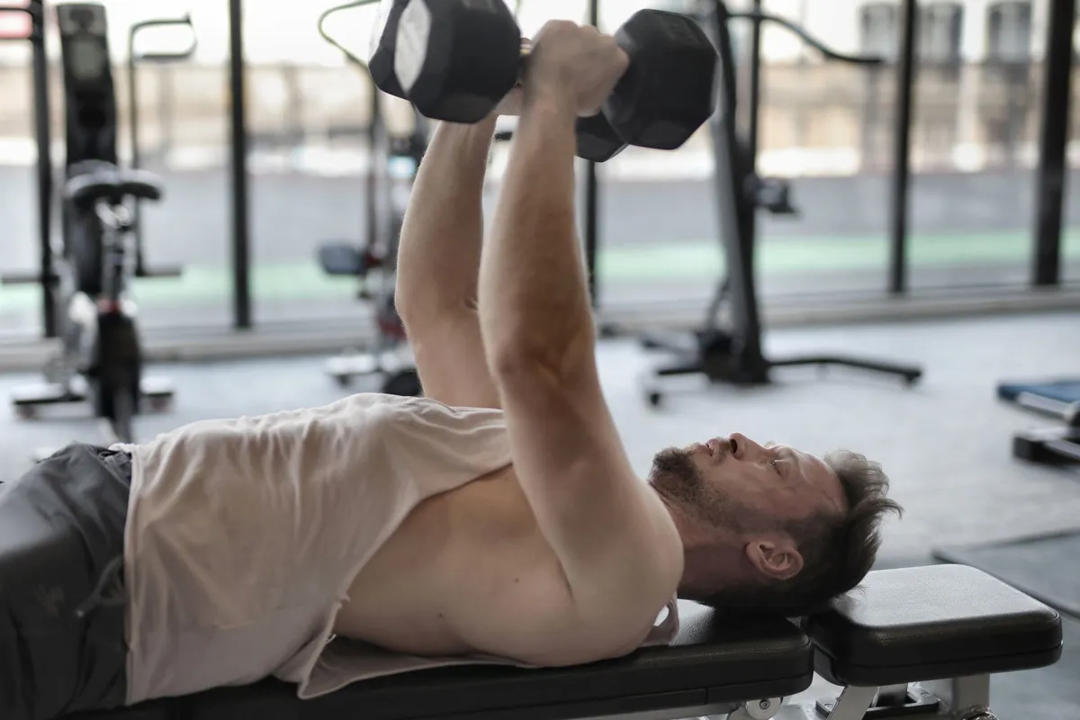 Man ligt op een trainingsbank en drukt twee dumbbells omhoog in de sportschool