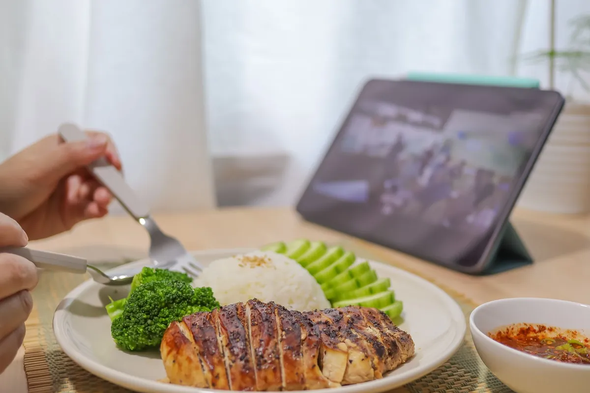 Iemand eet gegrilde kipfilet met rijst, broccoli en komkommer aan tafel
