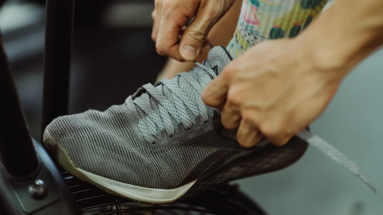 Close-up van handen die de veters strikken van een grijze sportschoen naast een fitnessapparaat