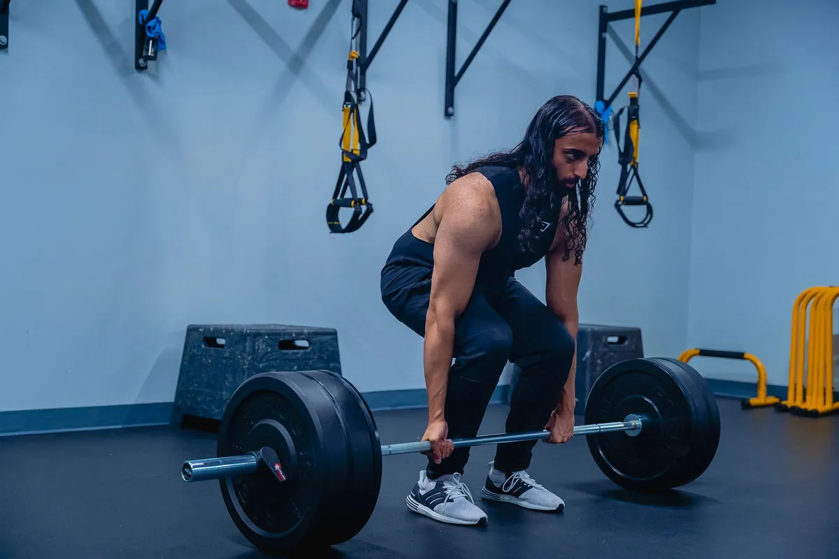 Man buigt vanuit de heupen voorover met een barbell net onder zijn knieën in een lichte sportschool