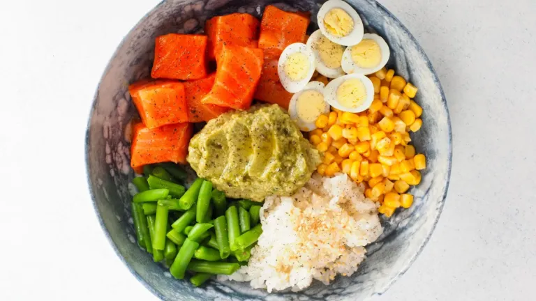 Eiwitrijke bowl met zalm, gekookte eieren, rijst, sperziebonen, mais en avocado van bovenaf gefotografeerd