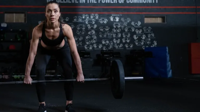Vrouw voert een romanian deadlift uit met een barbell op kniehoogte in een sportschool