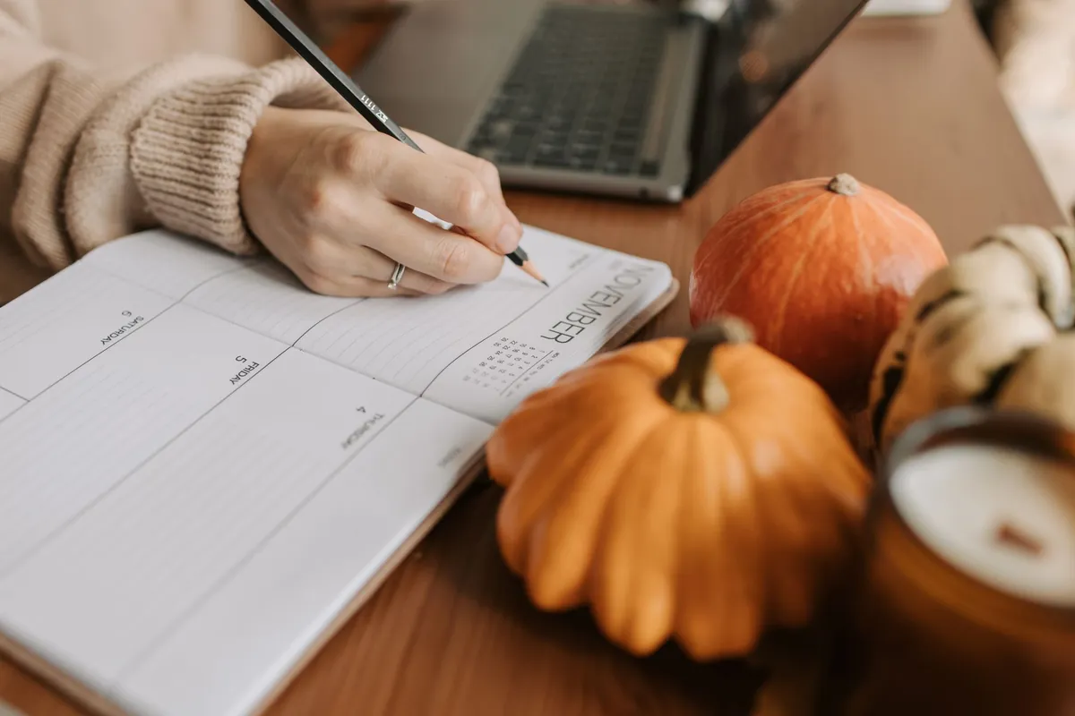 Iemand schrijft trainingsmomenten in een weekplanner op een houten tafel met pompoenen ernaast