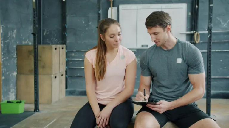 Personal trainer en sporter bespreken samen een trainingsschema op een tablet in de sportschool